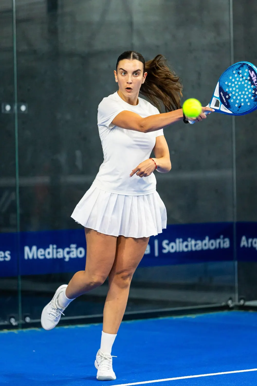 Jogadora de branco a bater uma direita num campo azul do Hype Padel Club, em Sendim.