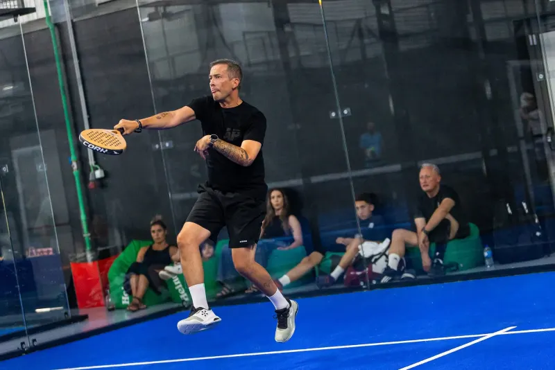 Jogo no Hype Padel Club, com o público sentado em puffs verdes junto ao vidro do campo.